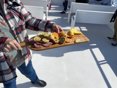 A contented passenger savoring a delectable charcuterie board on their private charter, relishing the freedom to bring their favorite food and drinks on board. The delightful spread includes an assortment of cured meats, artisanal cheeses, fresh fruits, and a selection of crackers, creating a perfect pairing with refreshing beverages of their choice. With the picturesque backdrop of Elkhorn Slough enhancing the experience, this passenger enjoys every bite and sip, making the most of the company, cuisine, and scenic journey.  #PrivateCharter #CharcuterieDelight #FoodAndDrinkFreedom #ScenicCruising